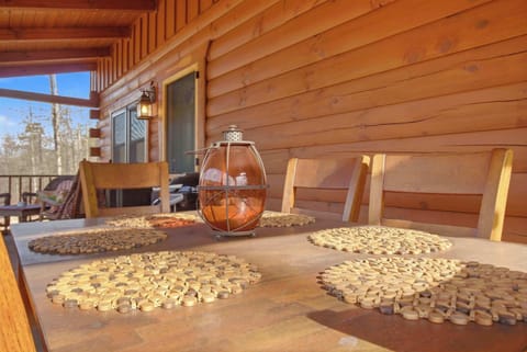 A cozy outdoor seating area on a rustic log cabin porch, featuring wicker furniture, colorful accent pillows, and a rocking chair, perfect for enjoying the wooded views in any weather.