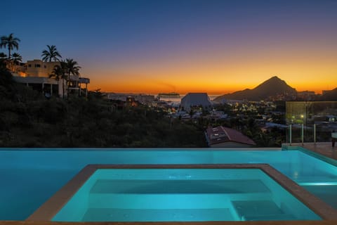 Stunning infinity pool overlooking tropical coastline at sunset, with dramatic mountain silhouettes and vibrant orange-purple sky creating the perfect evening backdrop.