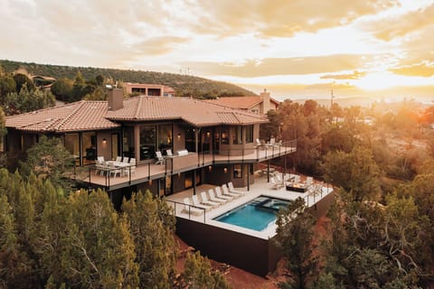 Modern hillside villa showcases stunning architecture with panoramic views during golden hour, featuring elegant pool terrace and natural landscape surroundings.
