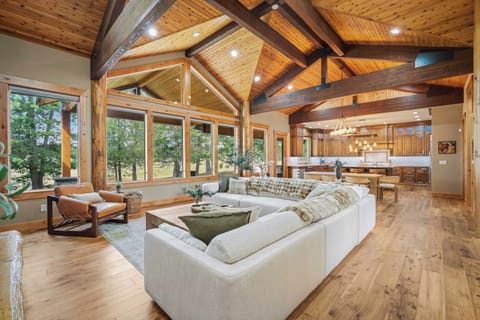 Relax in your stunning open-concept living space with soaring timber beams, floor-to-ceiling windows, and forest views creating the perfect mountain retreat atmosphere.