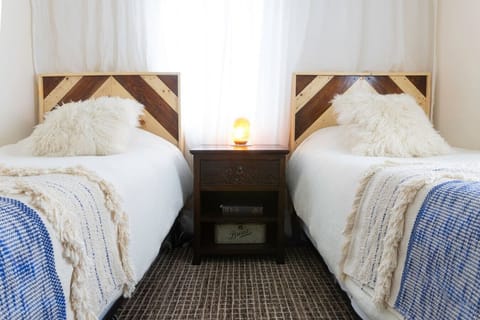 A cozy twin bedroom featuring two handcrafted Craftsman-style pine headboards and soft linen duvets. Warm wool carpets add comfort underfoot, creating a relaxed and inviting atmosphere. A beautiful wooden desk provides a perfect space for reading, writing