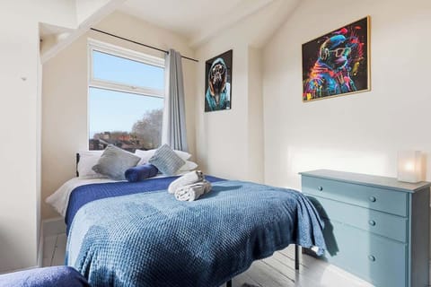 Bedding & Furniture: Features a larger bed with a blue textured bedspread and several grey pillows. It also contains a blue three-drawer dresser.