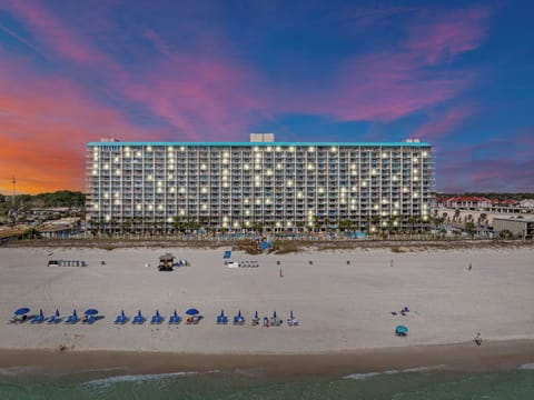 The Summit rises along the shoreline with its beachfront pools, palm‑lined deck, and sweeping views of the sugar‑white sands and emerald Gulf waters.
