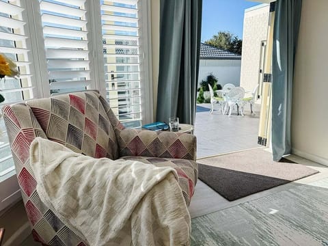 The armchair is where the day ends — plantation shutters open, sun on the tiles, the courtyard right there.