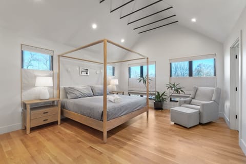 Unwind in your serene bedroom sanctuary with stunning four-poster bed, cozy reading chair, and peaceful views of nature through every window.