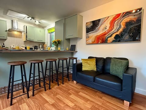 The open-plan lounge and kitchen offer shared seating on a navy sofa alongside bar stools at the breakfast bar beneath a large colourful wall piece.