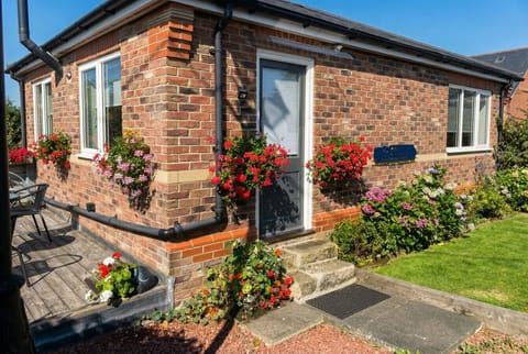 A sun-drenched brick cottage wrapped in vivid red geraniums welcomes you on arrival.