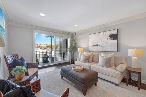 The living area is bright and inviting, featuring comfortable seating, coastal-inspired décor, and large sliding doors that open to a private balcony overlooking Harbour Town.