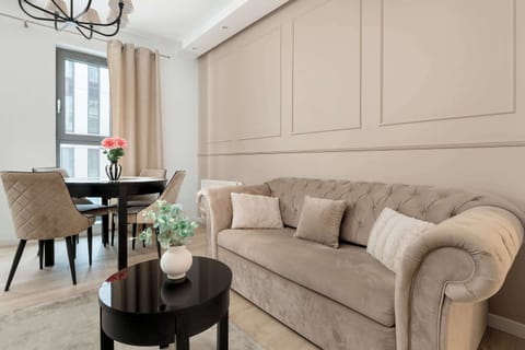 A cozy seating area with a comfortable beige sofa and decorative wall panels behind it. A small round coffee table with flowers adds a stylish touch to the interior. The soft color palette creates a calm and relaxing atmosphere.