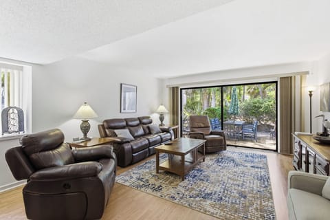 Supple leather seating and warm wood tones ground this spacious living room, where floor to ceiling glass opens to a lush garden view. Soft lamp glow and natural afternoon light create a serene setting for quiet evenings at home.