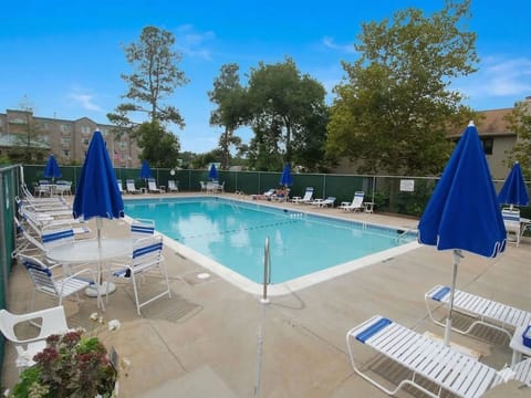 Relax by the community pool, surrounded by loungers and vibrant blue umbrellas, perfect for sunny days.