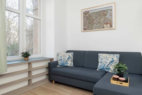 A comfortable seating area featuring a dark blue sofa placed against a white wall. Decorative pillows and a small coffee table sit in front of the couch. A window nearby allows natural light to brighten the space.