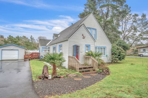 Charming coastal cottage with blue trim sits among towering trees, featuring a welcoming front deck and mature landscaping in a peaceful residential setting.