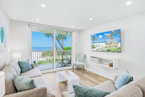 Your beachfront living room opens to stunning ocean views through sliding doors, where comfortable seating surrounds you with coastal tranquility.