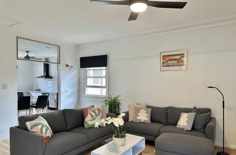 A spacious and inviting living room featuring a large grey sofa, wooden flooring, and a ceiling fan.