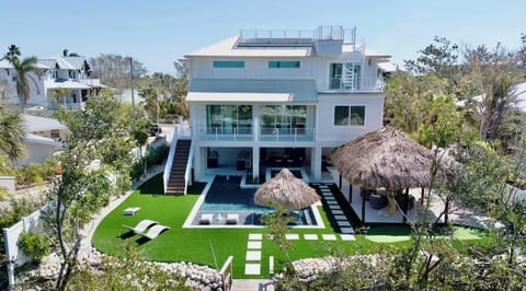 Modern waterfront villa featuring multiple levels, private pool, and tropical thatched pavilions set in lush landscaped grounds.