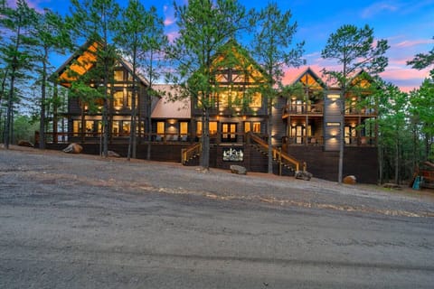 This stunning modern lodge nestled among tall pines glows beautifully at twilight with soaring ceilings and wraparound decks.