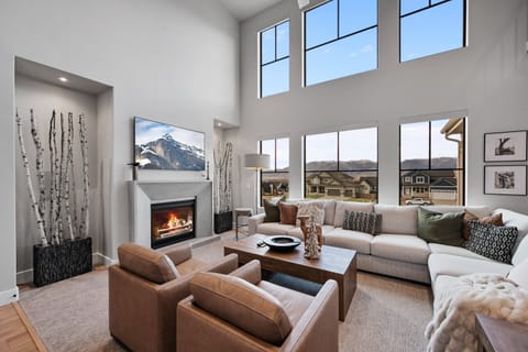 Expansive Windows with motorized blinds bring the beauty of the outdoors into the great room with plush furnishings a fireplace and smart TV