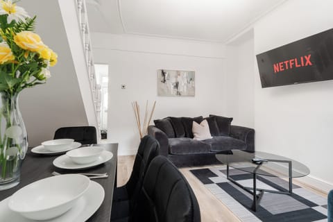 Bright and welcoming living space with a comfortable two-seater sofa and two lounge chairs. A wall-mounted Smart TV can be viewed from anywhere in the room. Dining area with a six-seater table is tucked neatly under the stairs just off the kitchen.