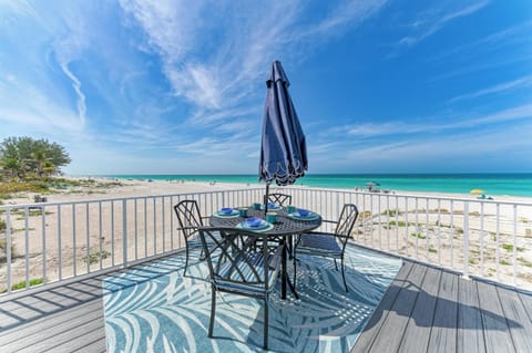A beachfront balcony with dining table overlooking pristine turquoise waters and white sand beach.
