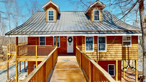 Charming log cabin with rustic red exterior and welcoming front deck surrounded by winter trees.