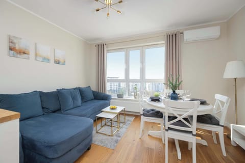 A bright living room with a blue sectional sofa, a white coffee table, and large windows letting in plenty of natural light.
