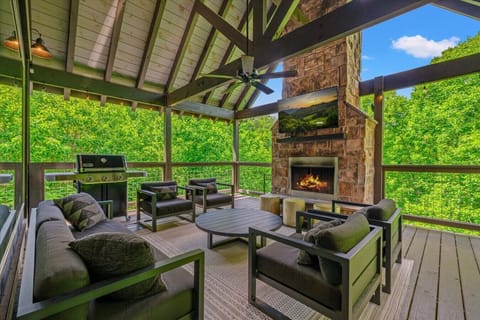 Unwind beneath soaring timber beams with a crackling fireplace, outdoor TV, and comfortable lounge seating surrounded by the trees.