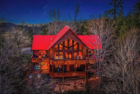 Stunning log cabin retreat glows warmly against a starlit mountain sky, surrounded by peaceful forest landscape.