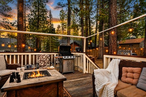 Spacious deck with a fire table, BBQ grill, and string lights for cozy evenings under the pines.