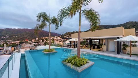 Rooftop pool with stunning mountain and city views overlooking a tropical hillside community at dusk.