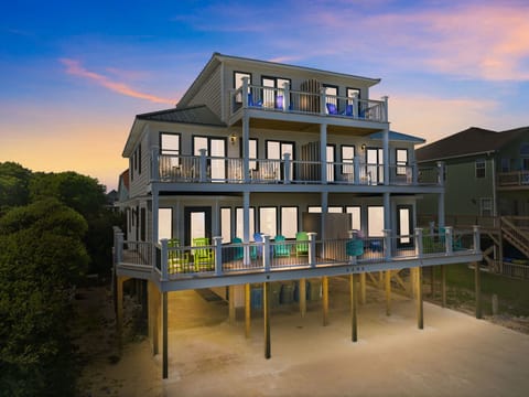 This coastal retreat features multiple levels of deck space with colorful seating and elevated stilt construction, set in a residential beachside neighborhood at sunset.