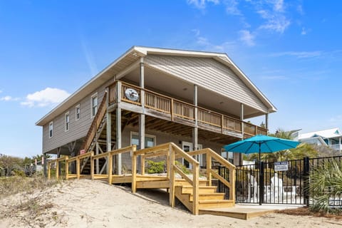 Coastal beach house with expansive wooden decking and pool area, perfect for seaside getaways under clear blue skies.
