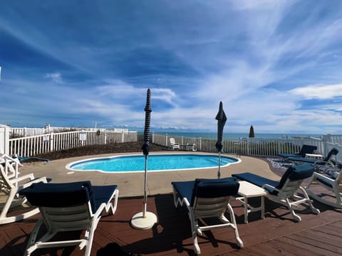 Rooftop pool deck offers panoramic ocean views with comfortable loungers and tables under expansive blue skies.
