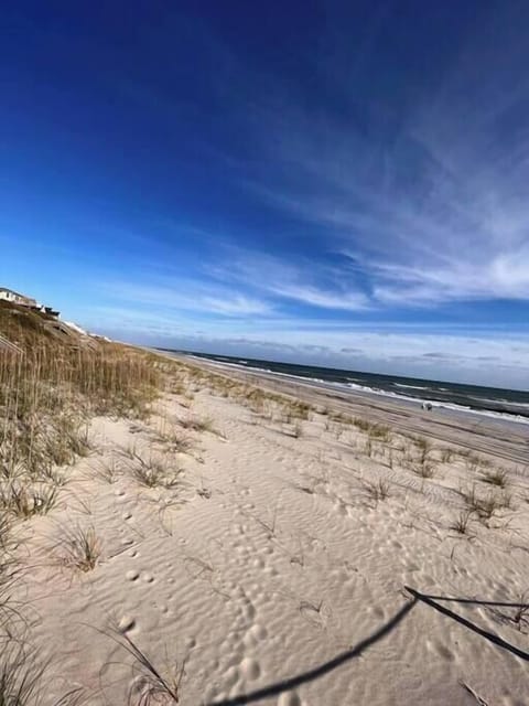 Pristine sandy coastline stretches beneath dramatic blue skies, with gentle dunes and beachside properties creating a perfect coastal setting.