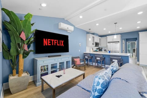Open-concept living and dining area with large Smart TV, streaming services, soundbar, mini-split A/C, and direct sightlines to the fully equipped kitchen