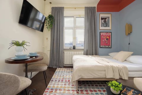 A bedroom corner with a neatly made bed and soft neutral bedding. A window nearby allows natural light to fill the room.