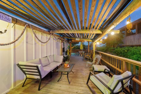 Unwind on the covered deck beneath the pergola, where soft seating invites relaxation and dining awaits just beyond—your open-air retreat framed by lush greenery and evening glow.