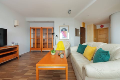 A cozy living area with a white sofa adorned with colorful cushions and a wooden coffee table against a backdrop of light-colored walls.