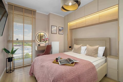 A bright bedroom features a large bed dressed in pink linens and a striking wooden accent wall behind the headboard.