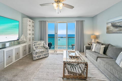 Coastal living at its finest — open, airy living room with a large-screen TV, Gulf views through the balcony doors, and stylish nautical touches.