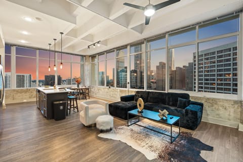 Unwind in a spacious open living area with panoramic sunset views and natural light. Perfect for relaxing on plush seating, entertaining, or enjoying a peaceful evening above the city skyline.