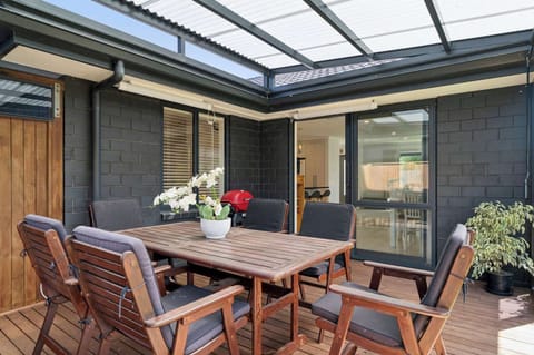 Covered outdoor entertaining deck with 6-seat timber dining setting and Weber BBQ — all-weather alfresco dining at this Rotorua holiday home