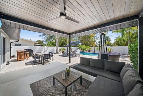 Covered lounge with ceiling fan, dining area, BBQ, and pool beyond.