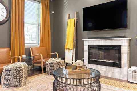 Inviting living room w/ a fireplace, TV & warm natural light pouring through yellow curtains.
