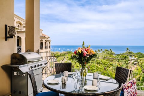 Balcony dining table with tropical flower centerpiece and sailboats anchored in Tamarindo Bay beyond.