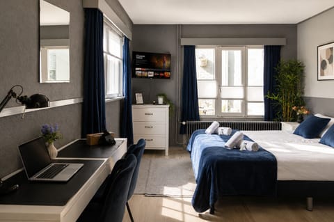 Modern bedroom with twin beds, workspace, wall-mounted TV, and large windows, offering a bright and functional stay.