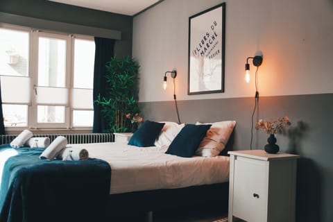 Cozy modern bedroom with soft lighting, large bed, decorative pillows, framed artwork, and a stylish plant creating a warm and inviting atmosphere.