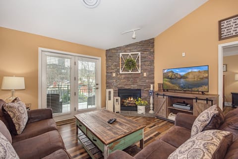 Cozy up in your rustic living room with stone fireplace, plush seating, and entertainment center for perfect evening relaxation.