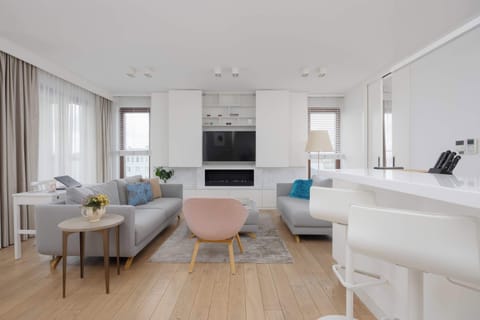 A stylish dining corner with a round table and soft pink chairs sits near large windows. The neutral palette and natural light create a calm and elegant atmosphere.