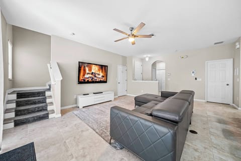 Unwind in the spacious living area with a comfy sectional sofa and a chic media console. Enjoy the natural light that fills the room, enhancing the warm tones and cozy vibe brought by the modern ceiling fan and decor.